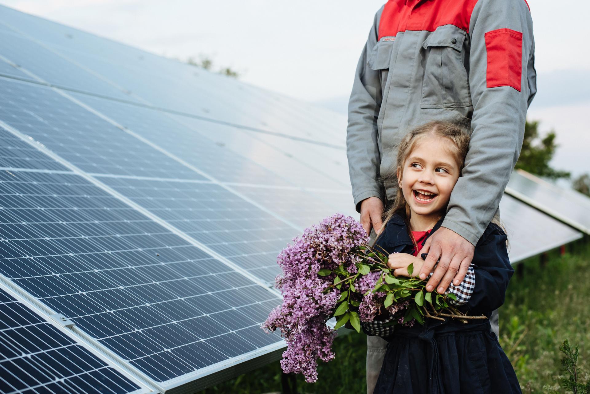 The child hugs the dad the electrician, on a background of solar panels. The engineer shows the girl the future of alternative energy and sustainable energy. The concept of ecology, a happy future.