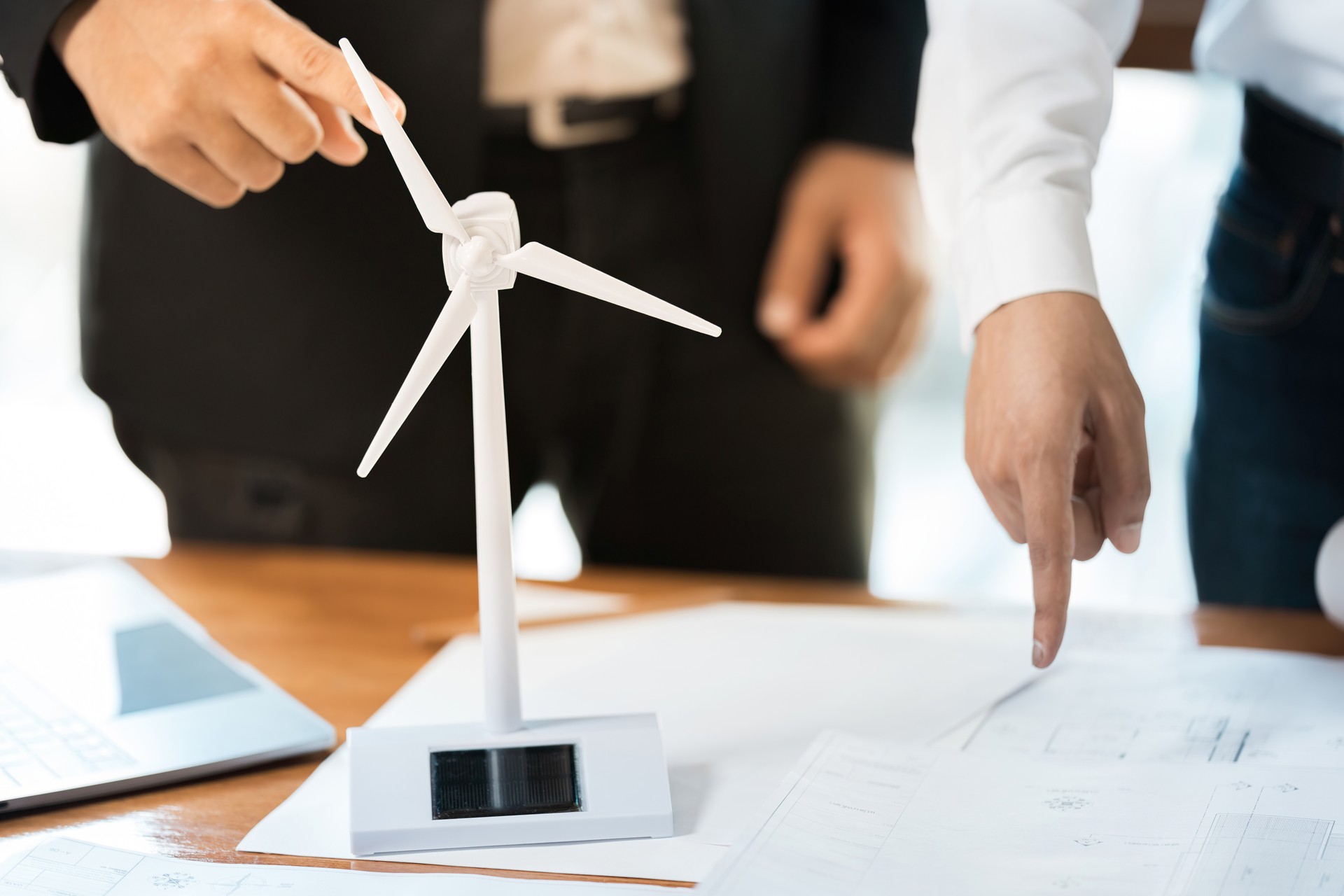 Close-up of a white energy wind turbine model on a workbench Hands of 2 Asian male architects pointing and blueprints of construction industry design in working office