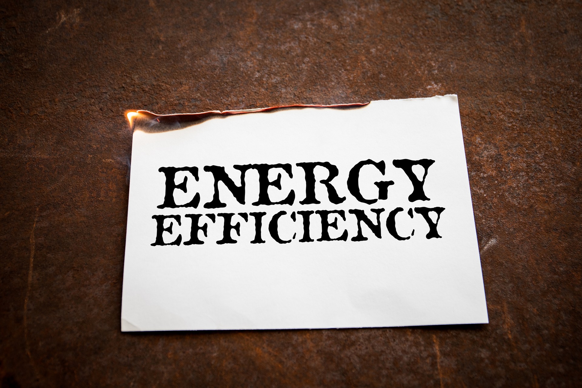 ENERGY EFFICIENCY. Burning paper with text on a rusty metal background